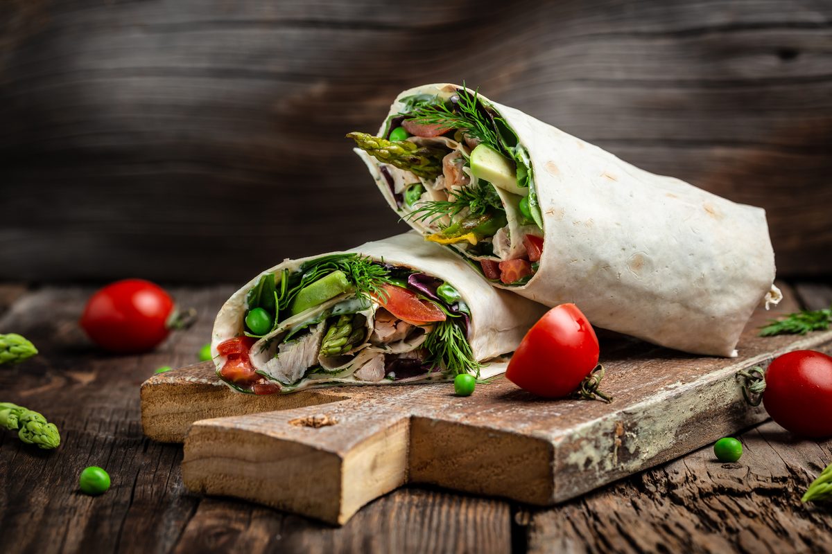 Two vegetable wraps on a wooden board with cherry tomatoes.