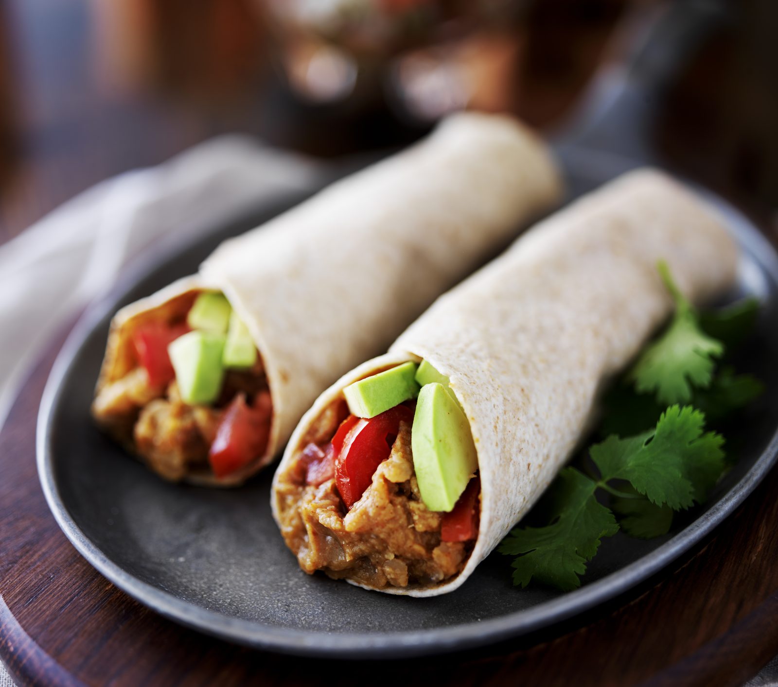 Two burritos on a dark plate, cut to show steak, black beans and rice.